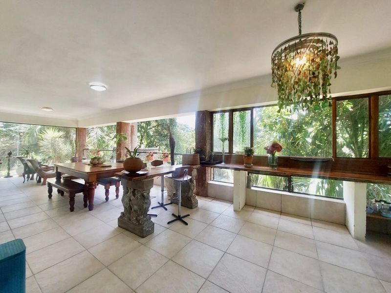 Spacious covered patio featuring tiled flooring, stone pillars, and a built-in wooden counter, offering a bright and airy space with large windows.