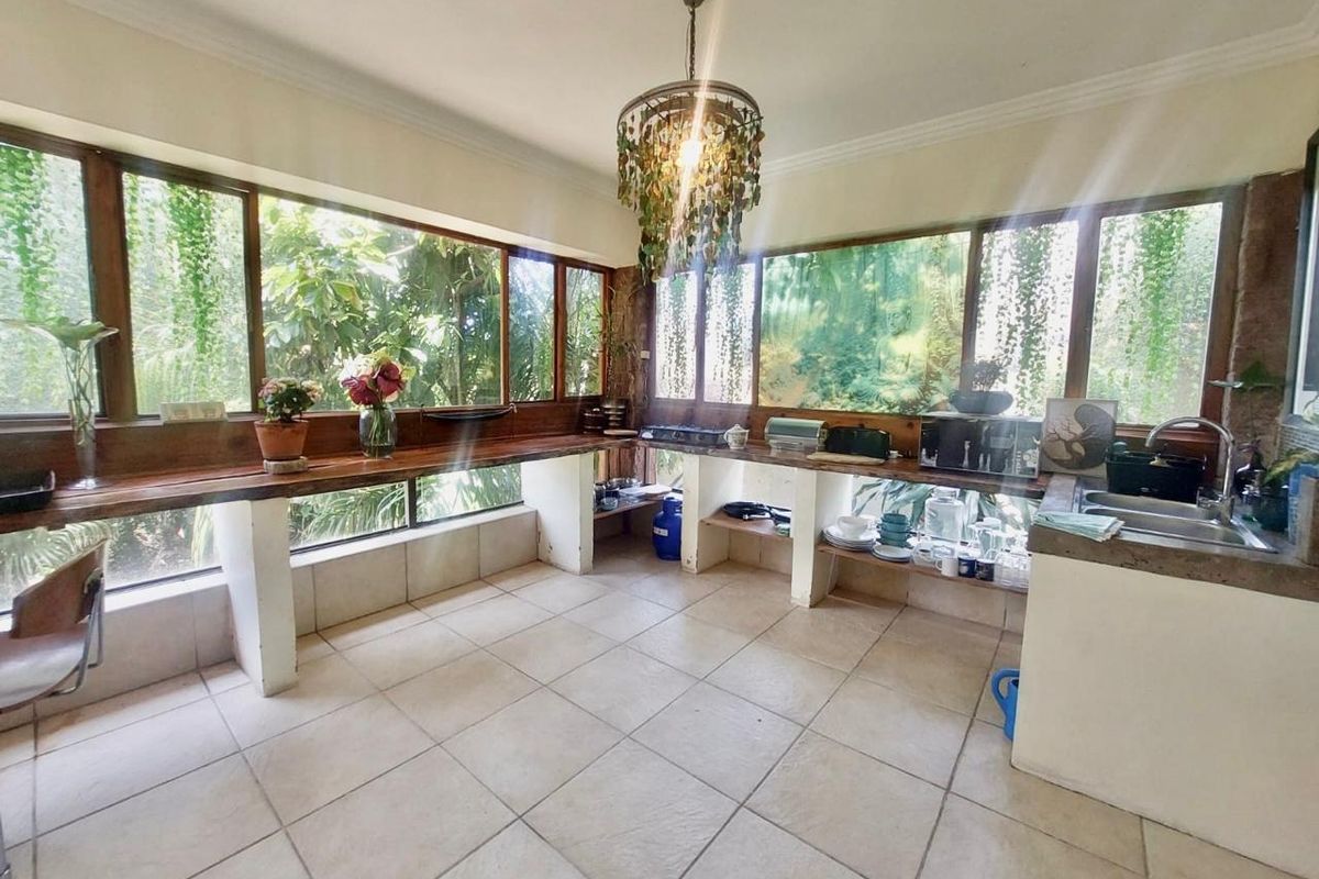 A sunlit kitchen featuring extensive wooden countertops, tiled flooring, and large windows overlooking greenery, offering a unique, open-concept prep and wash-up area.