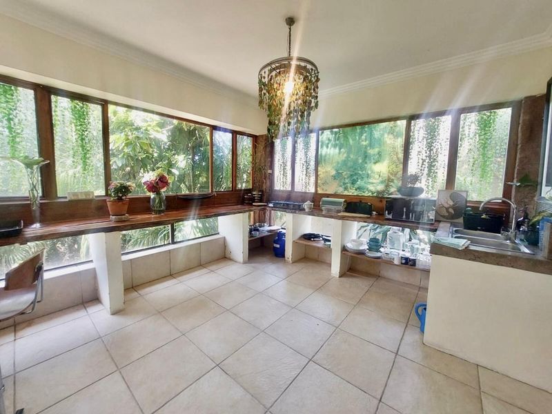 A sunlit kitchen featuring extensive wooden countertops, tiled flooring, and large windows overlooking greenery, offering a unique, open-concept prep and wash-up area.