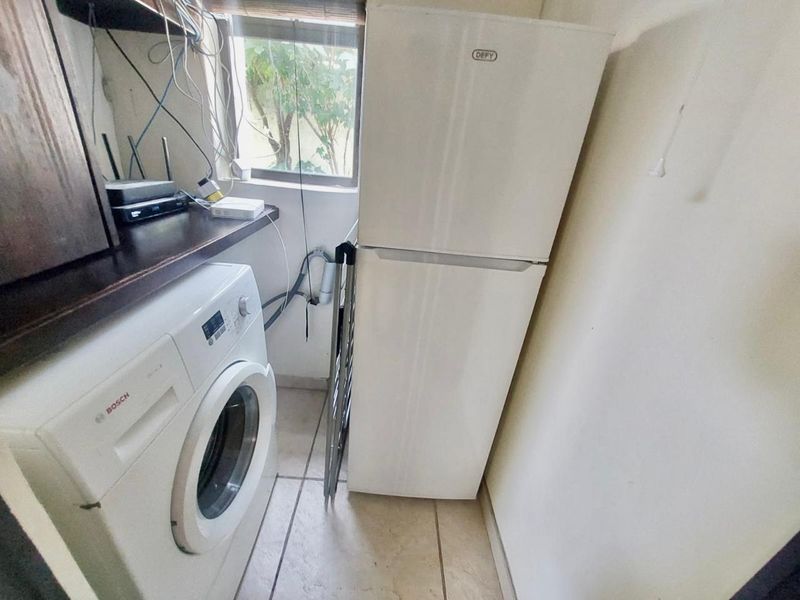 A compact laundry area featuring tiled flooring and dedicated plumbing connections for appliances, providing a functional utility space within the apartment.