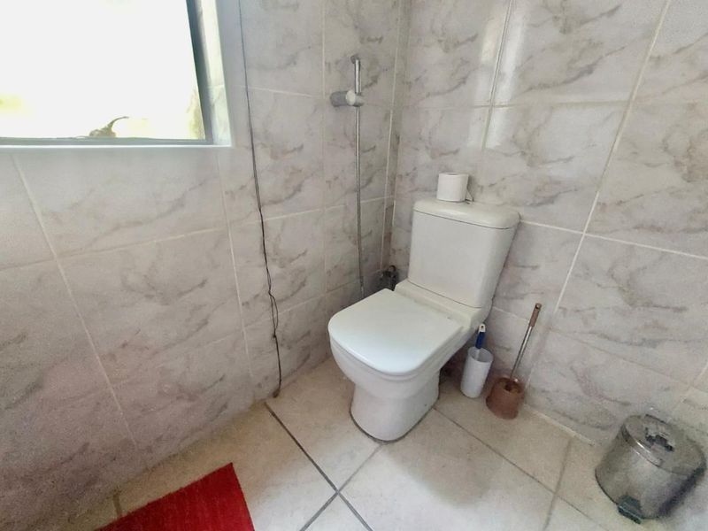 A functional bathroom featuring tiled walls and flooring, equipped with a standard toilet and a handheld bidet sprayer.