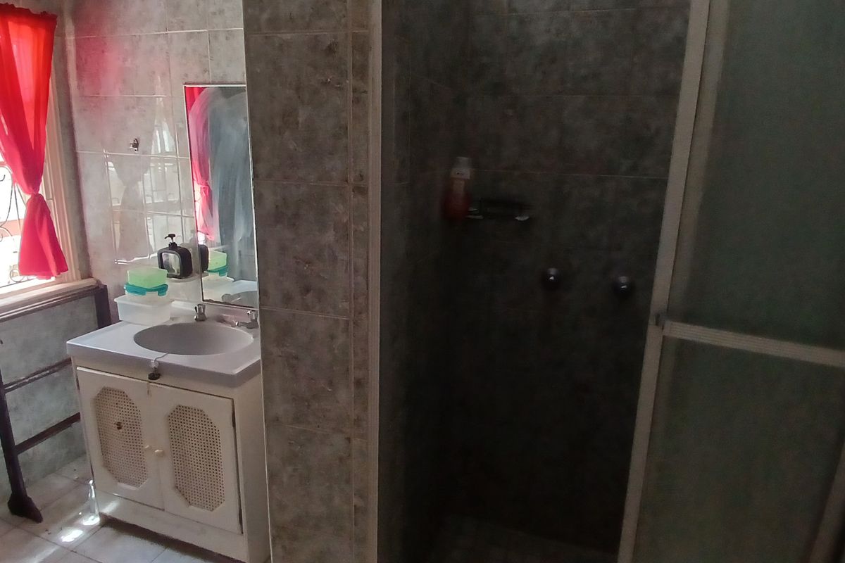 A functional bathroom featuring a vanity basin, a tiled shower enclosure, and natural light from a window with security bars.