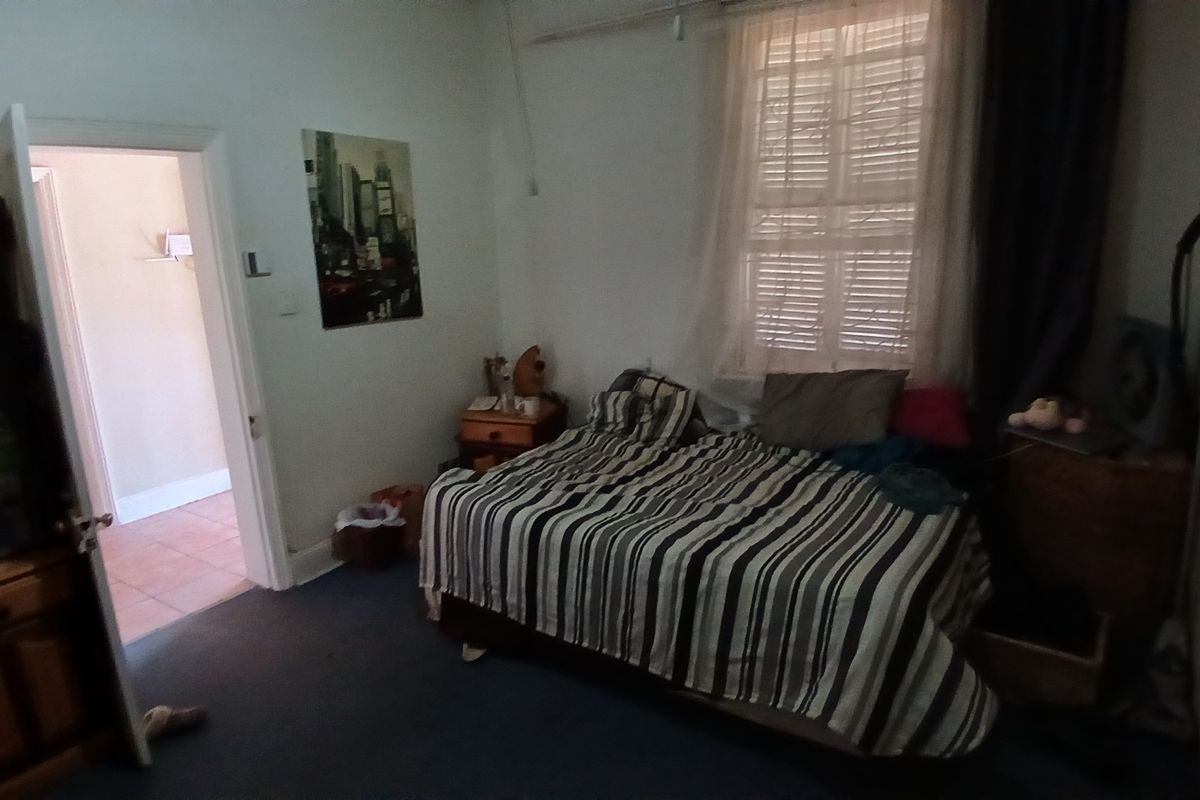 A bedroom featuring carpeted flooring, a window with security bars, and built-in storage, providing a functional space with potential for cosmetic updates.