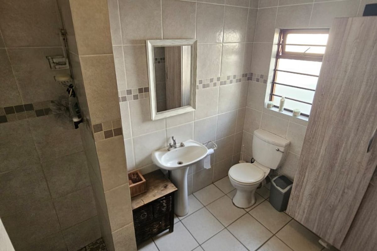 A functional bathroom featuring a pedestal basin, toilet, and a tiled shower enclosure with neutral wall and floor tiles.