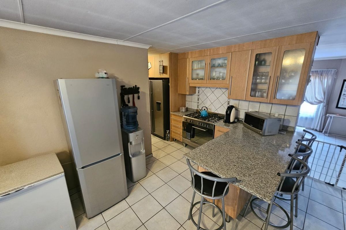 Functional kitchen featuring granite countertops, wooden cabinetry, gas hob, built-in oven, and tiled flooring with an integrated breakfast bar.