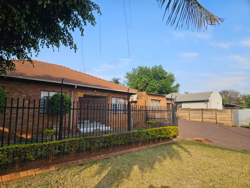 Front view of a face-brick house featuring a tiled roof, secure perimeter fencing, and a paved driveway leading to the entrance.