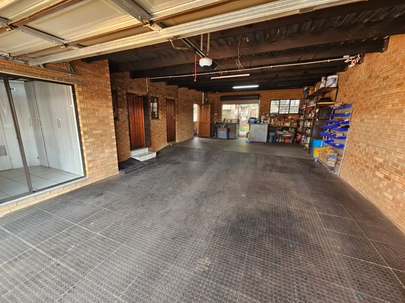 Spacious garage featuring exposed timber ceiling beams, durable brick walls, and rubber flooring, providing ample room for vehicle storage and workshop utility.