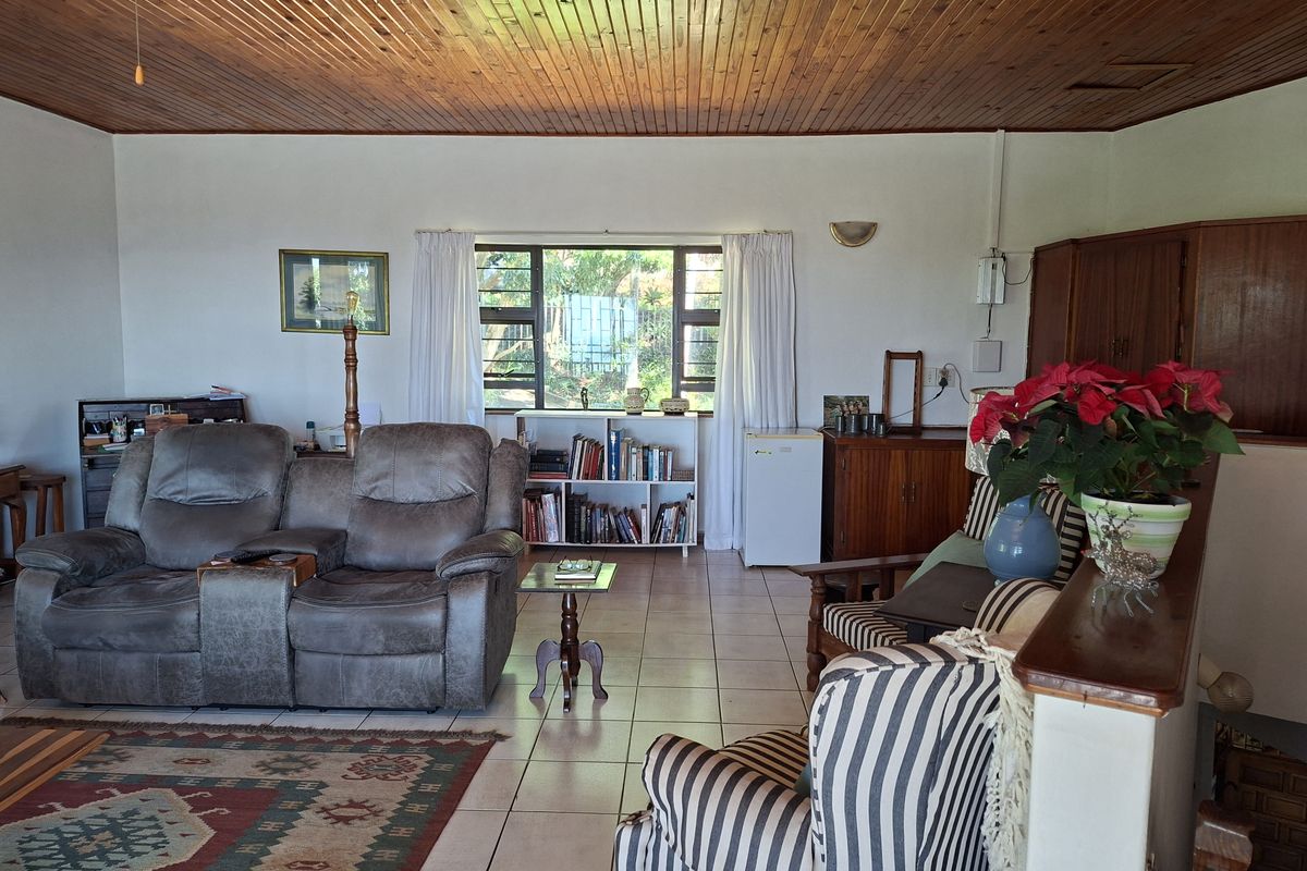 A spacious living area featuring a timber-clad ceiling, tiled flooring, and large windows that provide natural light and garden views.