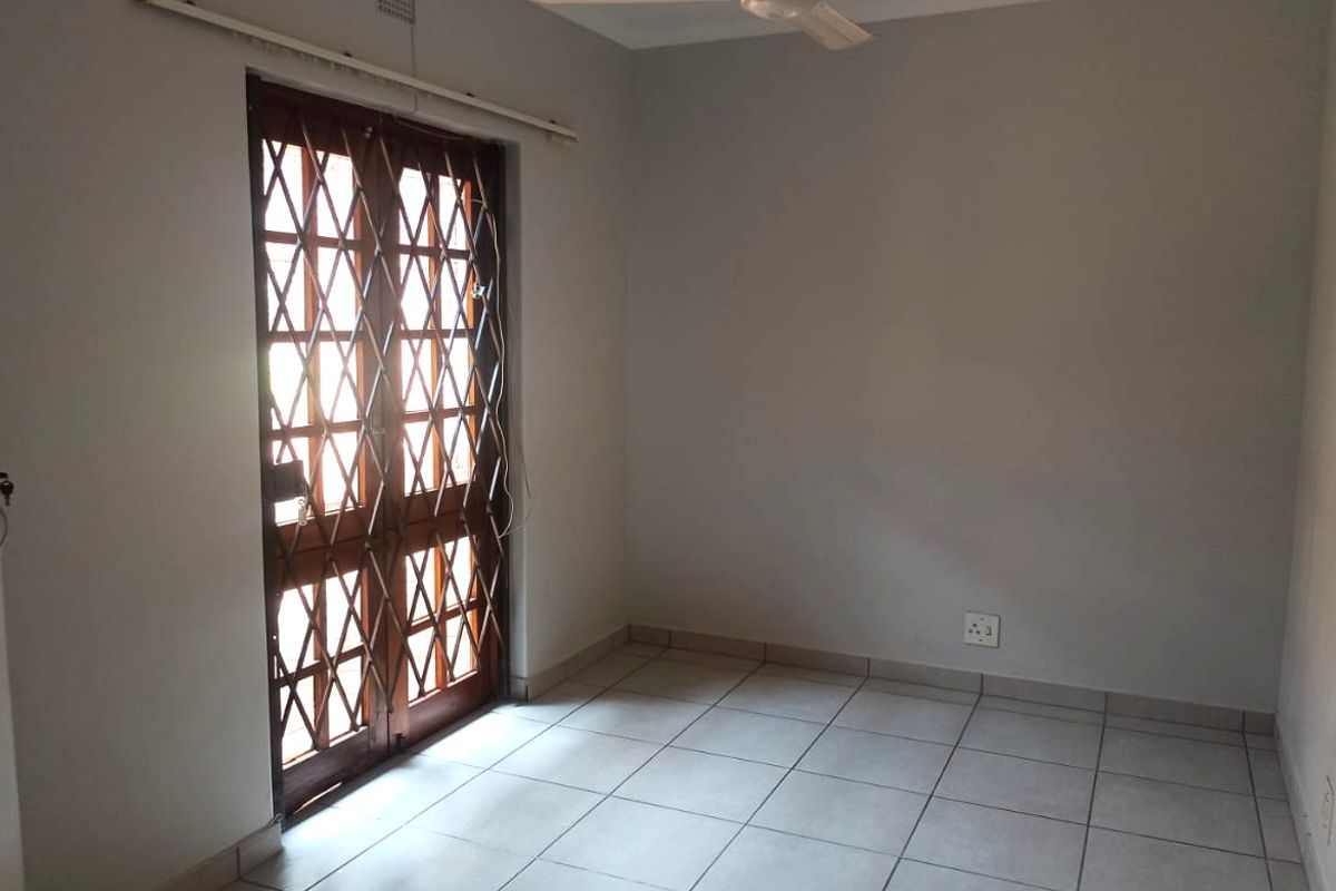 An empty bedroom featuring tiled flooring, a ceiling fan, and a wooden door with a security gate providing access to the exterior.