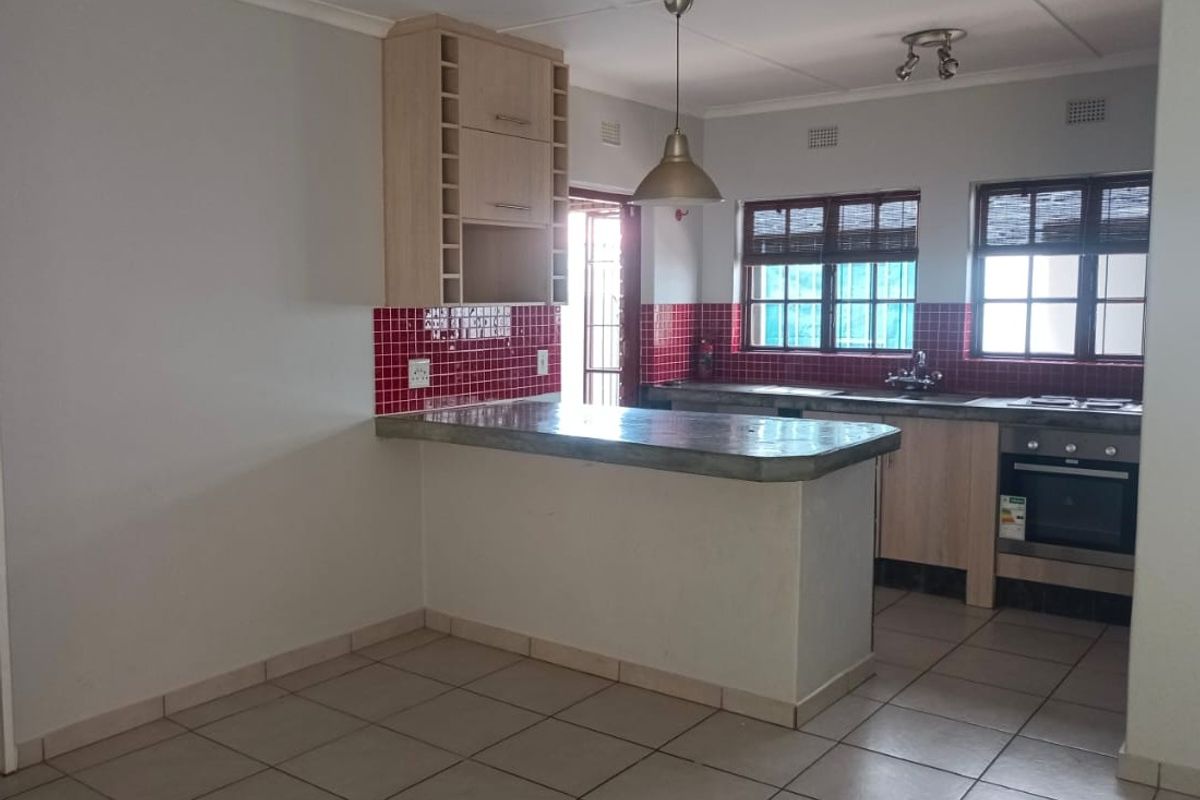 An open-plan kitchen featuring light wood cabinetry, a concrete breakfast bar, red tiled backsplash, and built-in oven with hob.