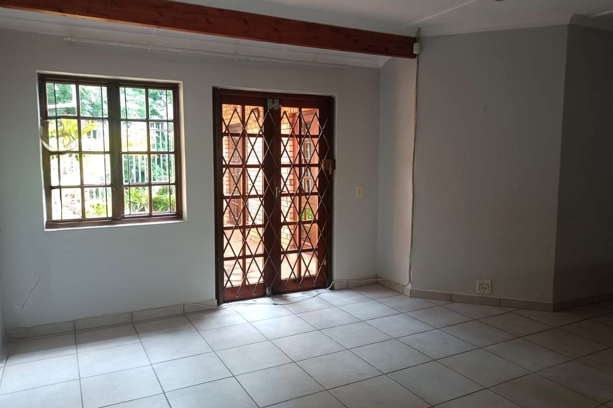 An empty living area featuring tiled flooring, a decorative wooden ceiling beam, and direct access to the exterior through a secure timber-framed door.