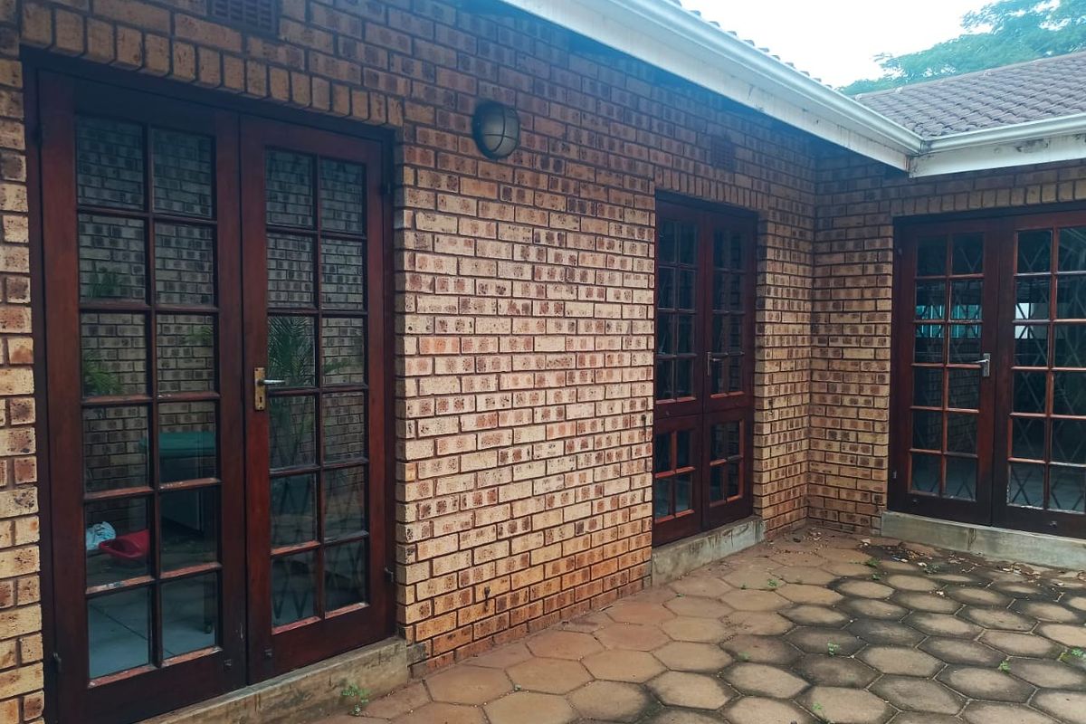 Rear exterior view of the apartment featuring a paved patio area, face brick facade, and multiple timber french door access points.