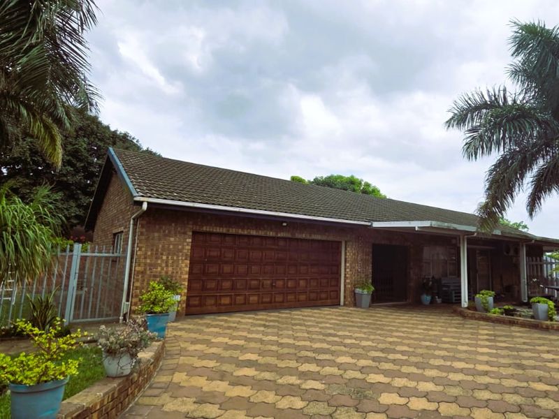 Front exterior view of a brick house featuring a paved driveway, a large sectional garage door, and established garden landscaping.