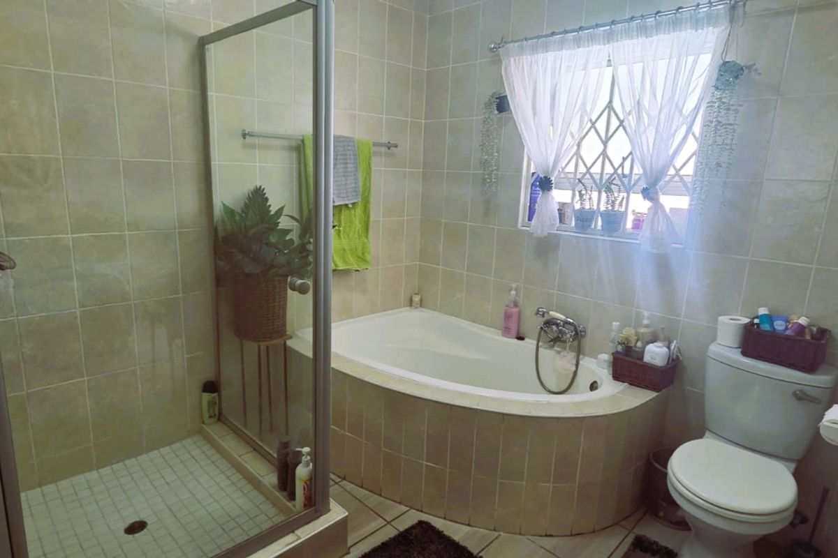 A functional bathroom featuring a built-in bathtub, separate shower enclosure, and tiled finishes throughout.