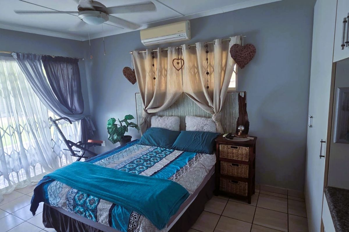A bedroom featuring tiled flooring, a ceiling fan, a wall-mounted air conditioning unit, and built-in cupboards with a vanity area.
