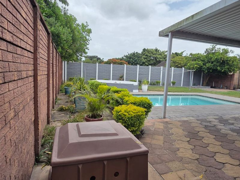 Outdoor pool area featuring a paved patio, covered entertainment space, and secure brick and precast concrete boundary walls.