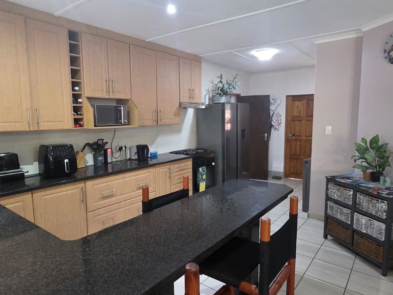 A functional kitchen featuring light wood cabinetry, dark granite countertops, a breakfast bar, and tiled flooring.