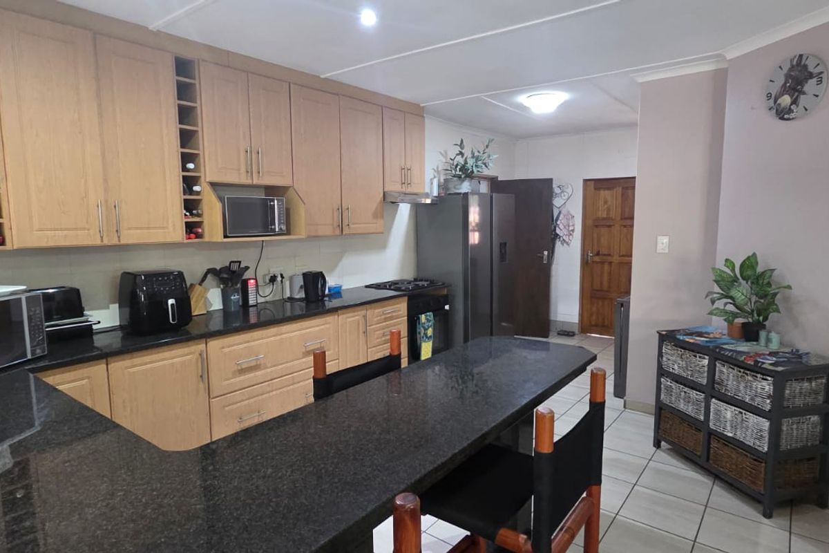 A functional kitchen featuring light wood cabinetry, dark granite countertops, a breakfast bar, and tiled flooring.