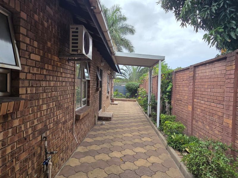 A side exterior view of the property featuring a paved walkway, face brick walls, and a covered patio area.