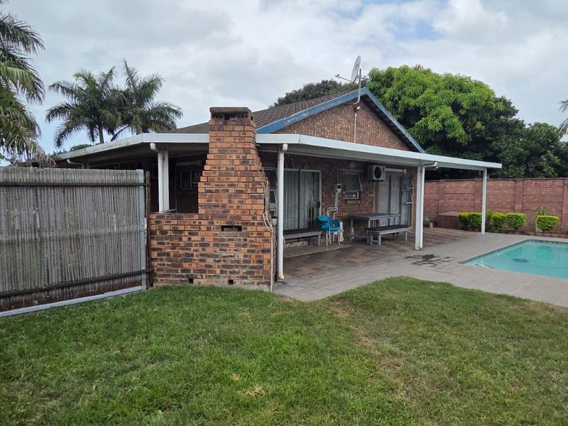 Rear exterior view featuring a swimming pool, paved patio area, and a brick built-in braai structure set within a private garden.