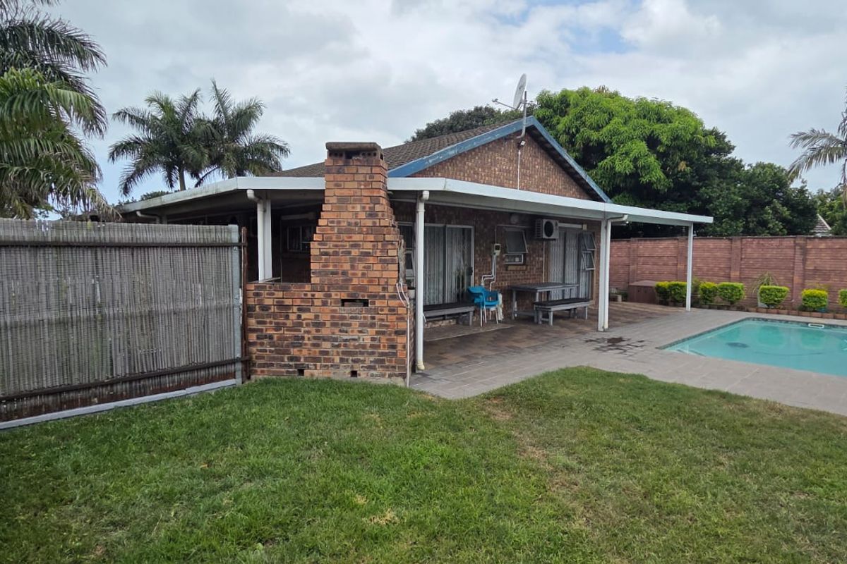 Rear exterior view featuring a swimming pool, paved patio area, and a brick built-in braai structure set within a private garden.