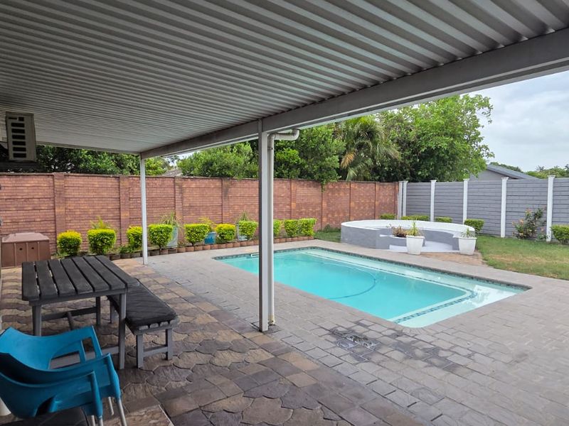 Outdoor entertainment area featuring a covered patio, swimming pool, and a private garden enclosed by brick and concrete boundary walls.