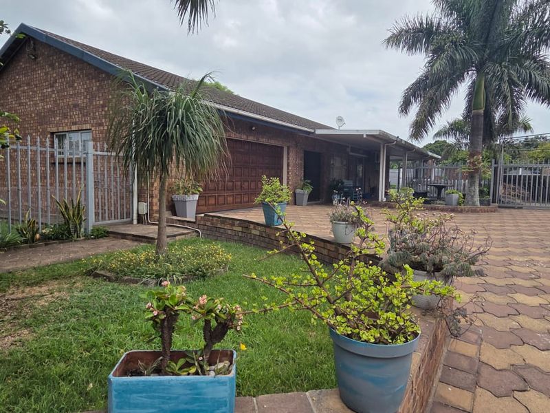 Front exterior view of a brick house featuring a paved driveway, double garage, and established garden area with perimeter fencing.