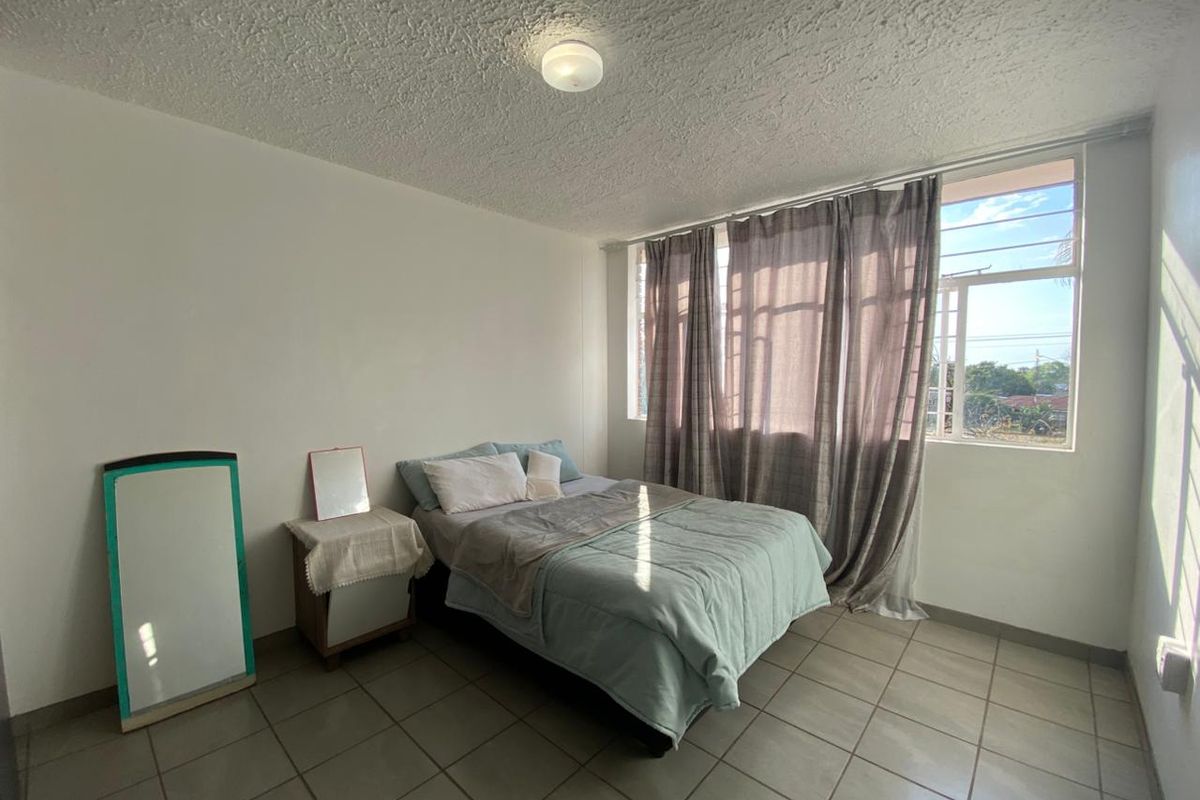 A functional bedroom featuring tiled flooring, a textured ceiling, and a large window that provides natural light.