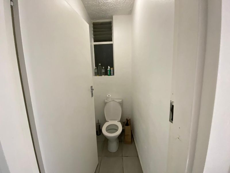A compact, functional bathroom featuring a standard toilet, tiled flooring, and a louver window for ventilation.