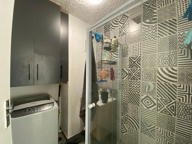 Compact bathroom featuring a shower enclosure with patterned wall tiles and built-in overhead cabinetry for storage.