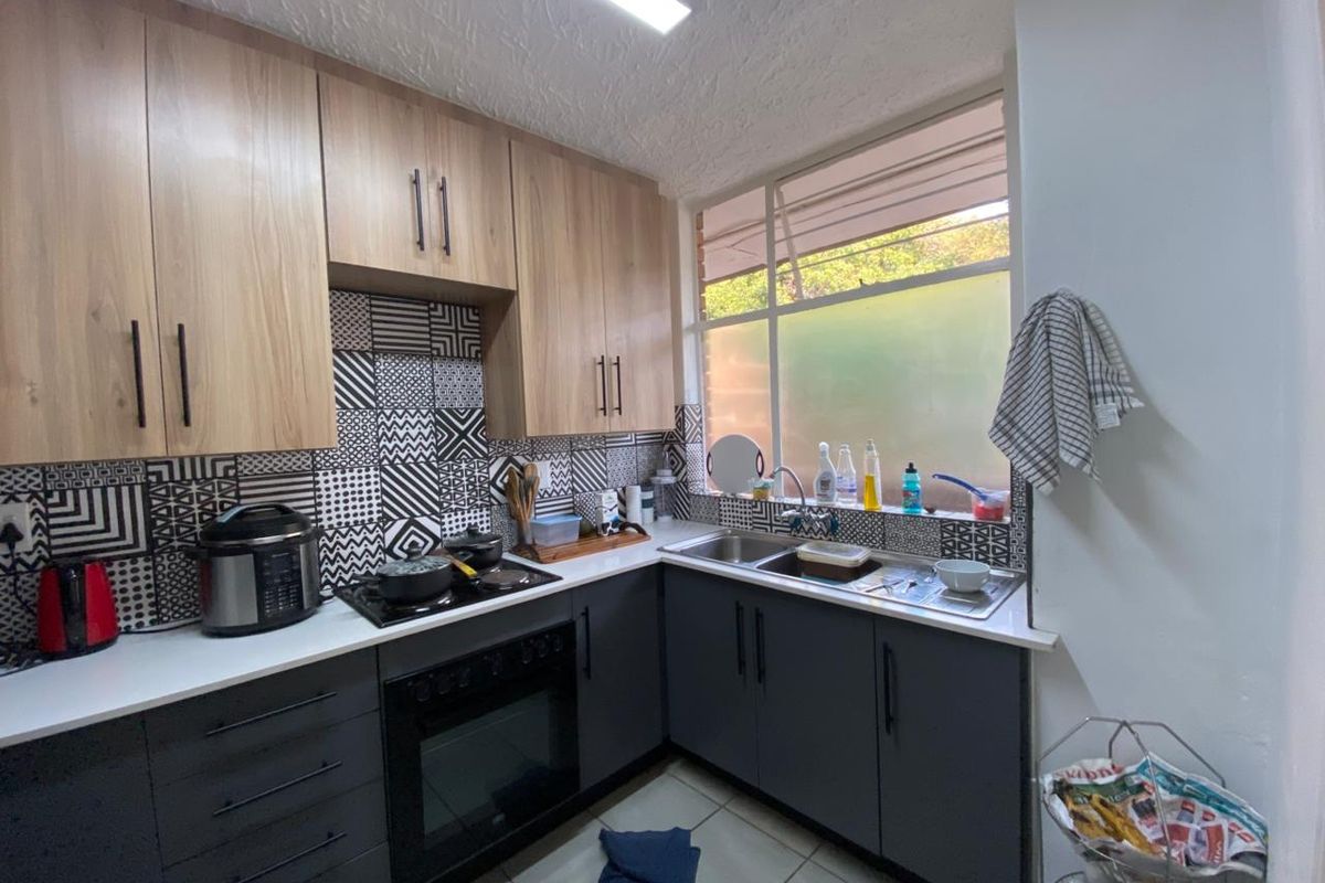 A functional kitchen featuring modern two-tone cabinetry, a built-in oven and hob, tiled backsplash, and a stainless steel double sink with ample counter space.