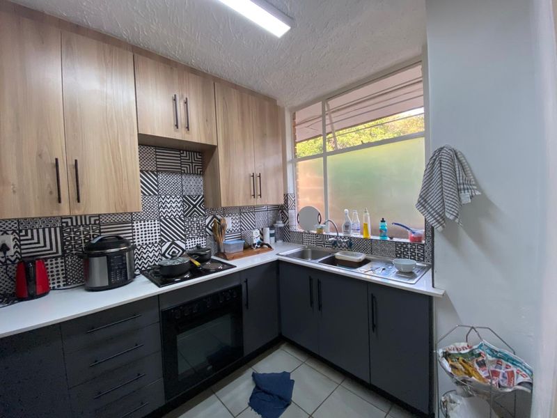 A functional kitchen featuring modern two-tone cabinetry, a built-in oven and hob, tiled backsplash, and a stainless steel double sink with ample counter space.