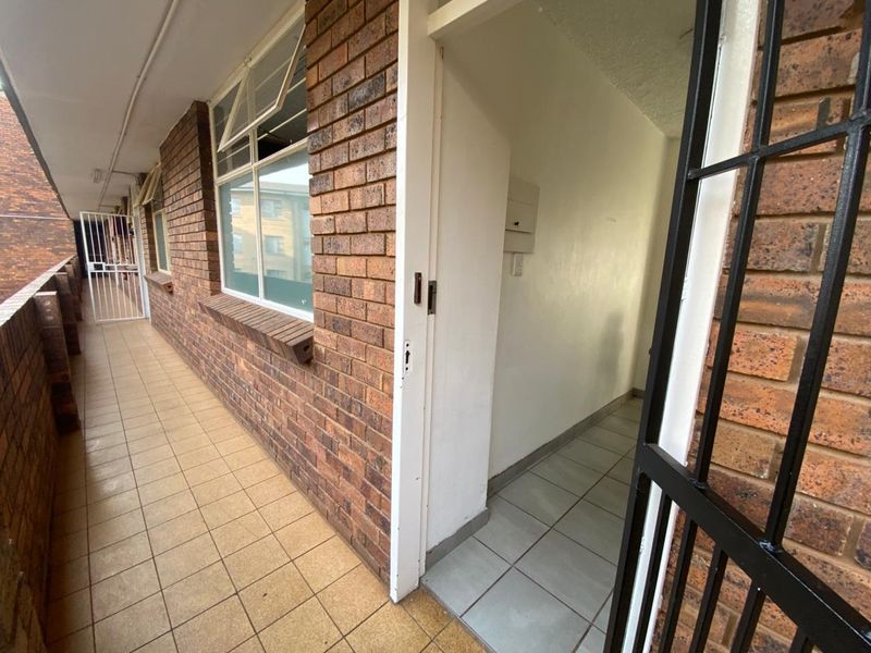 An exterior balcony featuring brick walls, tiled flooring, and a security gate, providing access to the apartment interior.