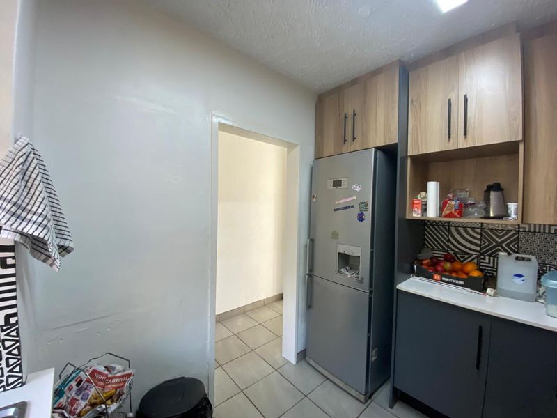 A functional kitchen area featuring modern two-tone cabinetry, patterned tiled backsplash, and tiled flooring, leading into an adjacent utility space.