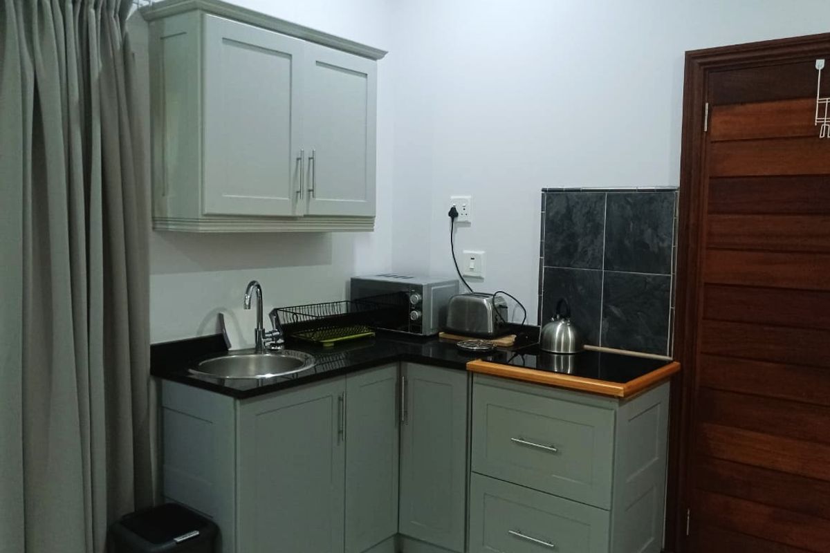 Compact kitchen area featuring grey built-in cabinetry, granite countertops, a stainless steel sink, and a tiled splashback.