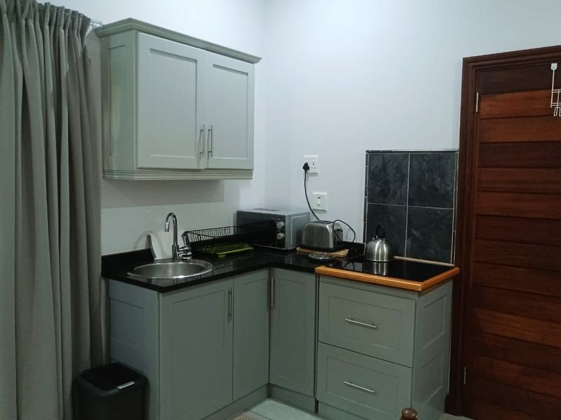 Compact kitchen area featuring grey built-in cabinetry, granite countertops, a stainless steel sink, and a tiled splashback.