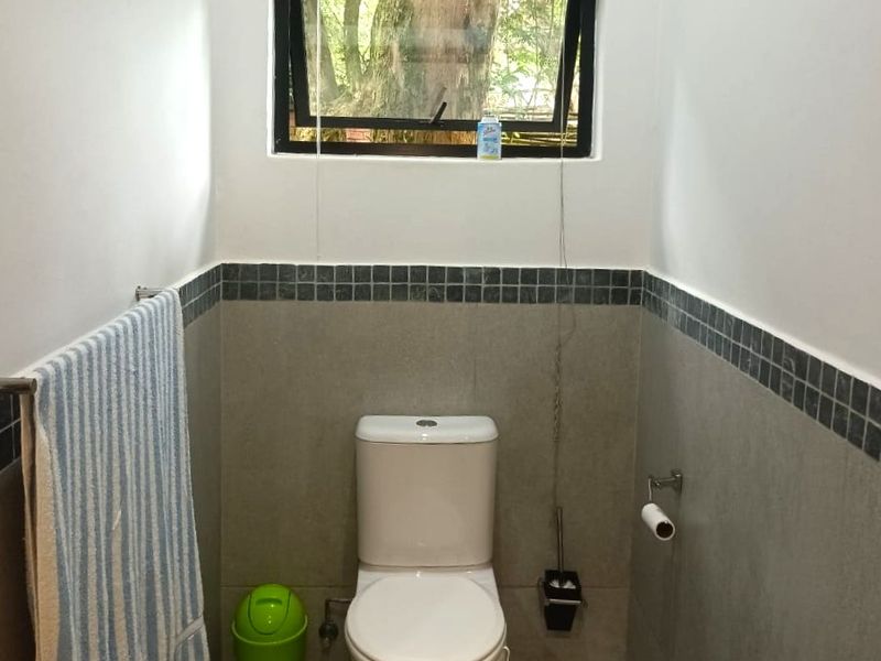 A compact bathroom featuring neutral wall and floor tiling, a standard toilet, and a top-hung window for natural ventilation.