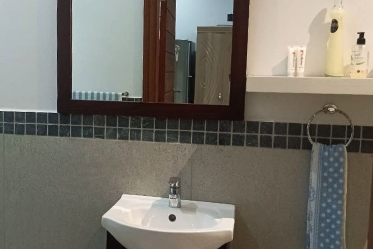 A functional bathroom vanity area featuring a modern ceramic basin, dark wood-finish cabinet, wall-mounted mirror, and tiled splashback.