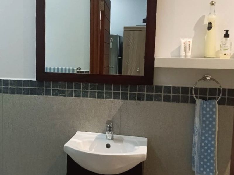 A functional bathroom vanity area featuring a modern ceramic basin, dark wood-finish cabinet, wall-mounted mirror, and tiled splashback.