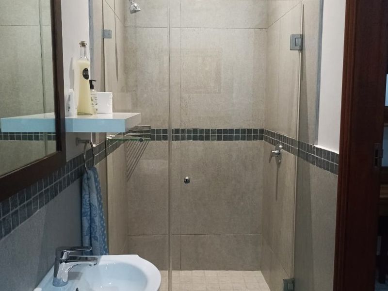 A modern bathroom featuring a glass-enclosed shower with tiled walls, a vanity basin with a mixer tap, and a wall-mounted mirror.