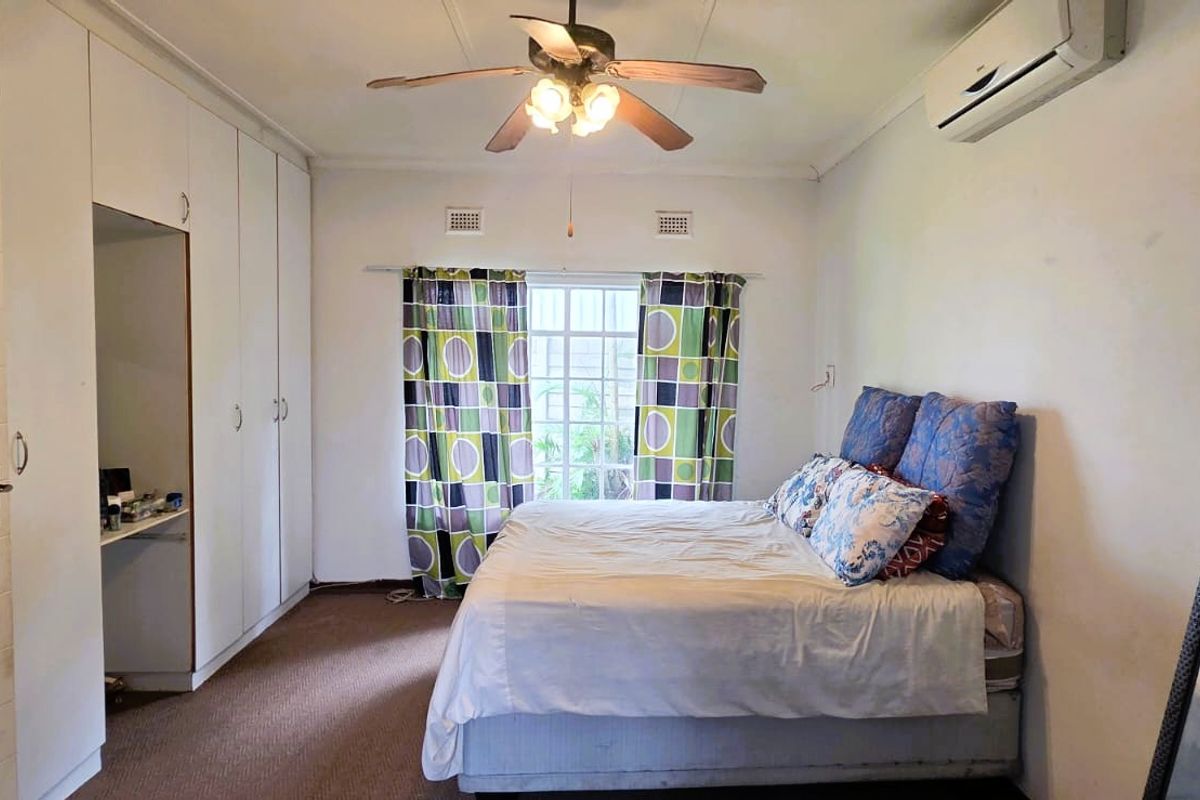 A bedroom featuring built-in floor-to-ceiling wardrobes, a ceiling fan, and a wall-mounted air conditioning unit.
