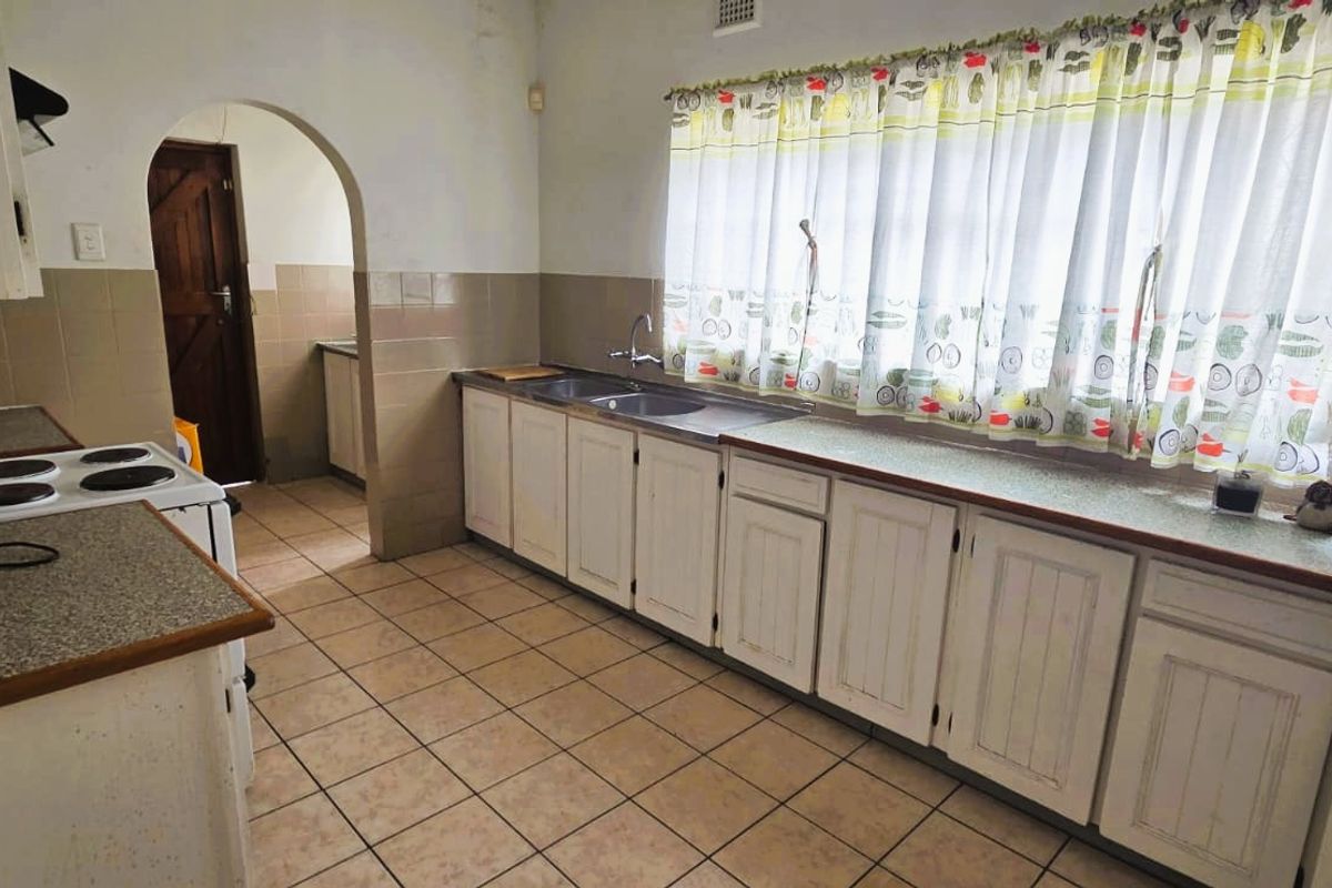 A dated kitchen featuring tiled flooring, laminate countertops, and traditional white cabinetry with an arched doorway leading to an adjacent space.