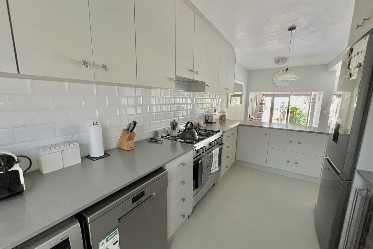 Modern kitchen featuring white cabinetry, subway tile backsplash, quartz countertops, and stainless steel appliances, flowing into an adjacent living area.