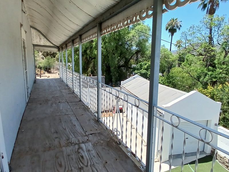 An elevated outdoor balcony featuring a corrugated metal roof and wrought iron balustrade, overlooking the rear garden and garage area.