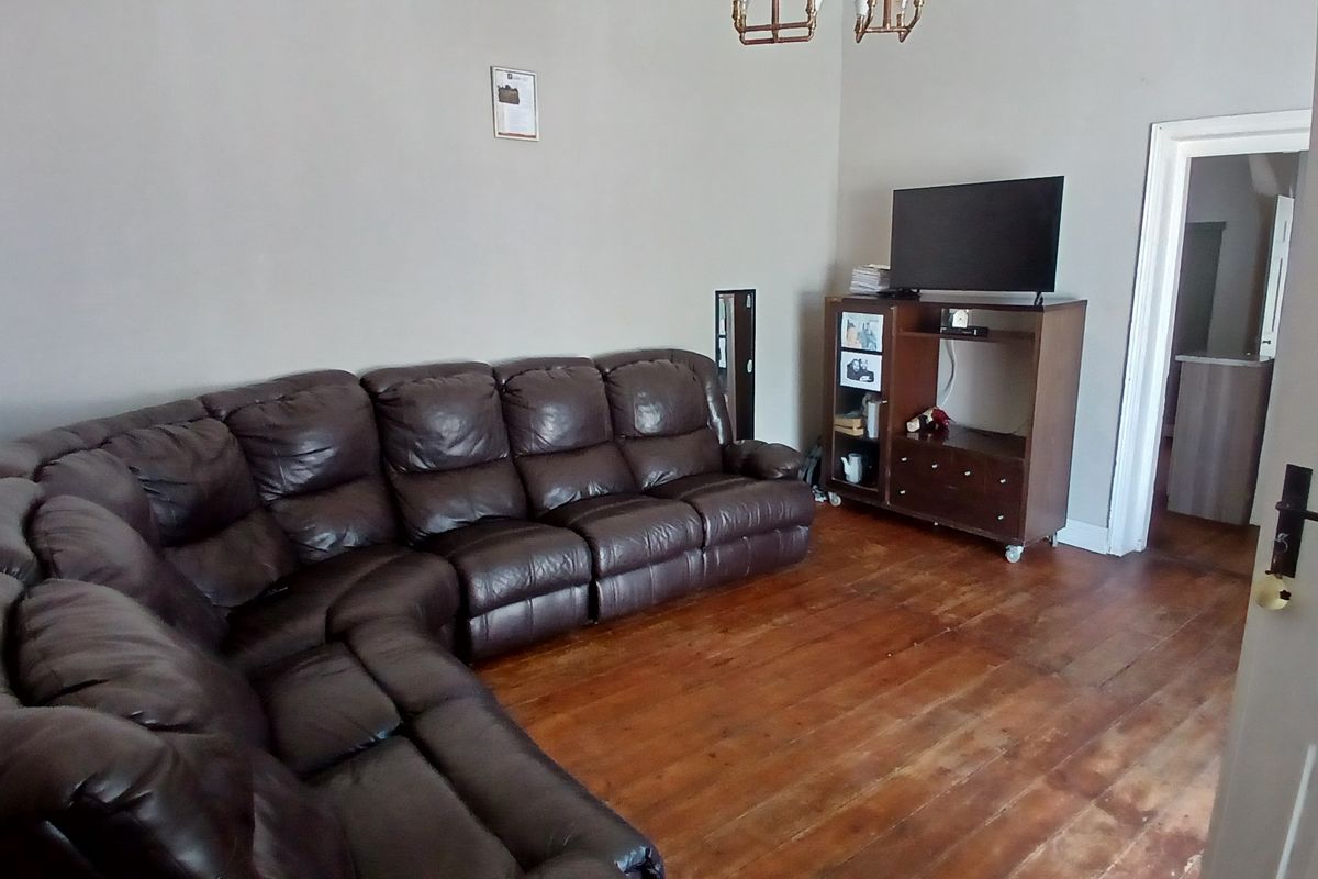 A living room featuring original hardwood flooring and neutral wall tones, offering a functional space ready for cosmetic updates.
