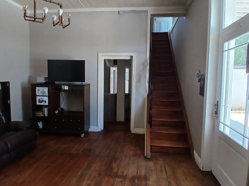 Living room featuring original timber flooring, a timber staircase, and a glass-panelled entrance door, providing access to the upper level and adjacent rooms.