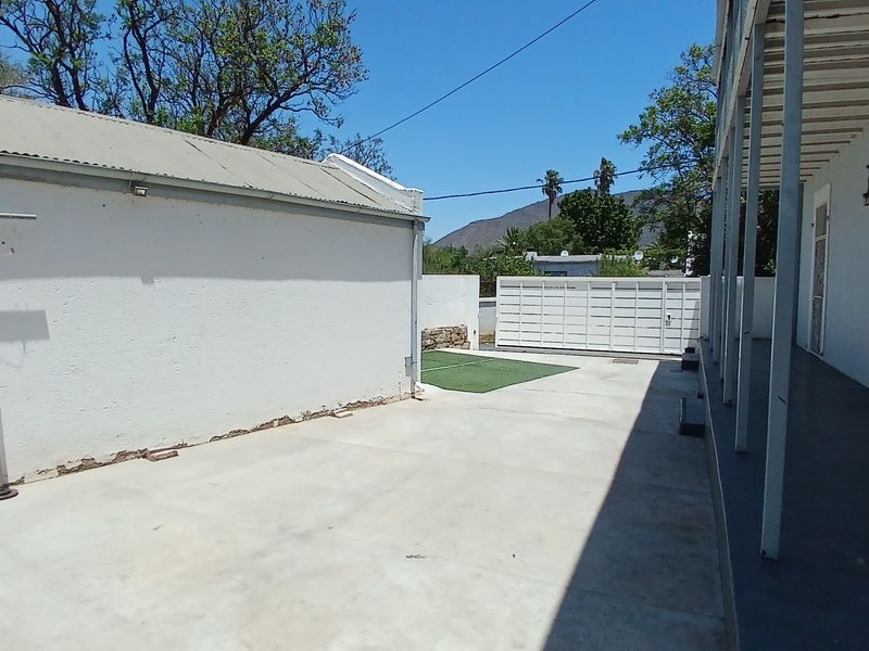 Rear exterior area featuring a concrete patio, covered veranda with structural pillars, and a secure perimeter wall with gate access.