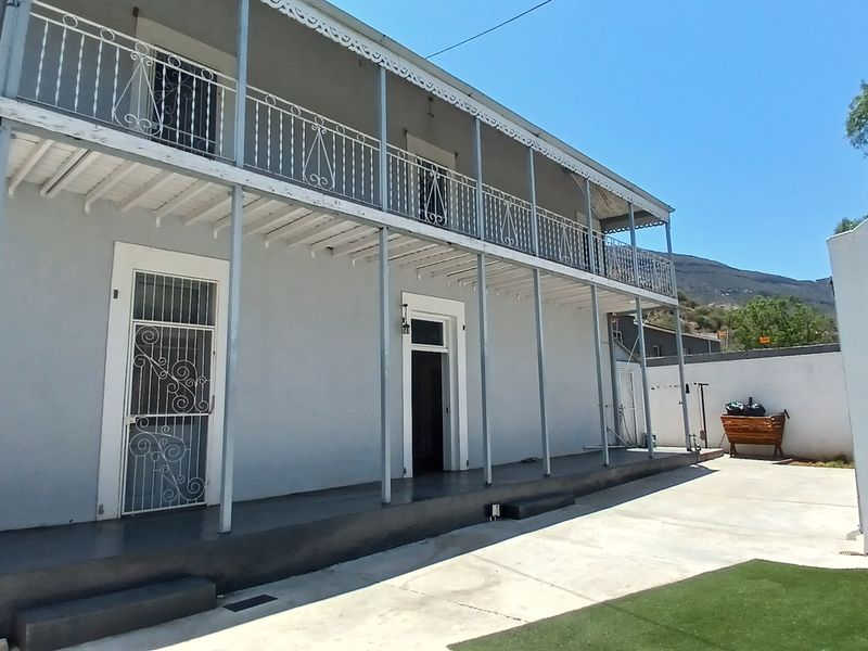 Rear view of a double-story house featuring a full-length veranda with wrought iron railings, a concrete patio area, and an adjacent garage.