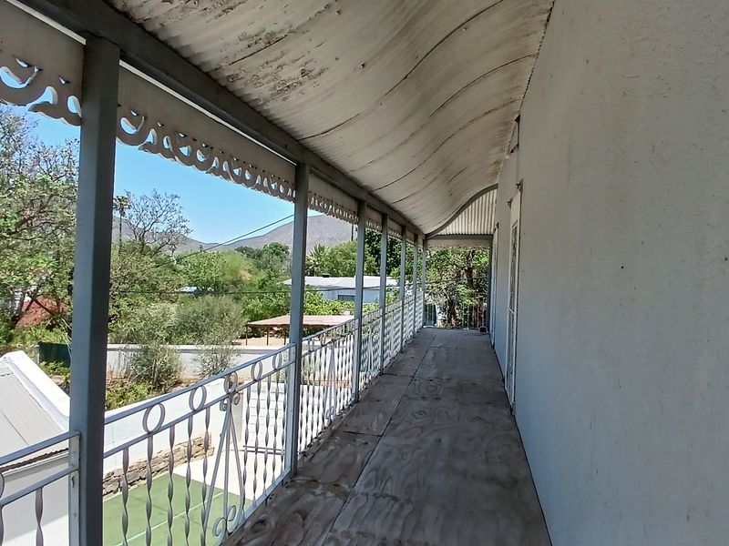 An elevated balcony featuring a corrugated metal roof, decorative metal fretwork, and a wrought iron balustrade with views of the surrounding landscape.