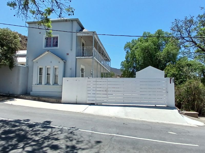 Front exterior view of a two-story house featuring a white sliding gate, concrete driveway, and an upper-level balcony with metal railings.